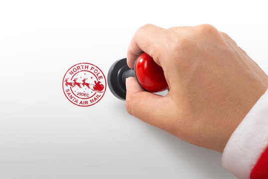Hand in Santa suit stamping red North Pole Santa air mail rubber stamp on white background