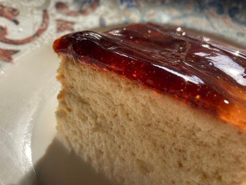 Close-up of tres leches cake slice with glossy red jam glaze on a decorative plate in sunlight