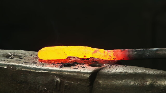 Craftsman hammers incandescent metal on industrial anvil surface closeup. Bright sparks emphasize energy and precision of blacksmith forging