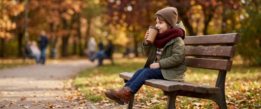 Child with a takeaway cup and woolen scarf on a park bench. Cozy autumn outing