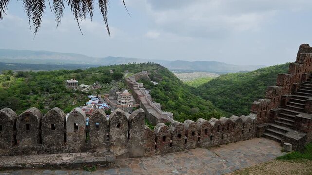 A parapet with arrow openings overlooks the long wall winding across green ridges at Kumbhalgarh Fort on an Udaipur excursion.