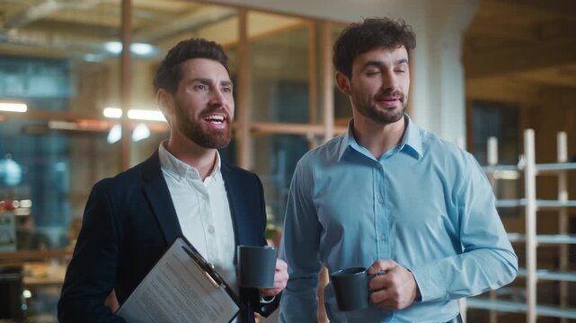 Calm happy two Caucasian business men drinking coffee beverage relaxing at morning in office. Smiling cheerful businessmen male partners drink tea smile optimistic together thinking relaxing at break
