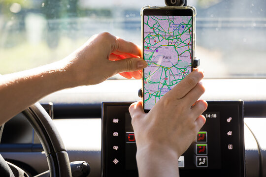 Hand adjusts a smartphone with a city map mounted on a car windshield holder. A navigation concept shows driving guidance, route planning and modern GPS technology on the road.