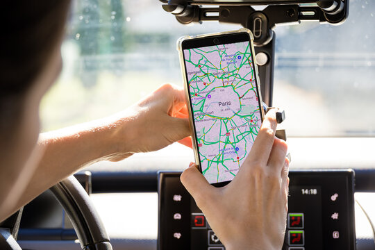 Hand adjusts a smartphone with a city map mounted on a car windshield holder. A navigation concept shows driving guidance, route planning and modern GPS technology on the road.