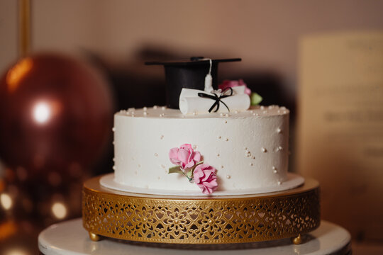 White graduation cake decorated with a diploma and a cap.