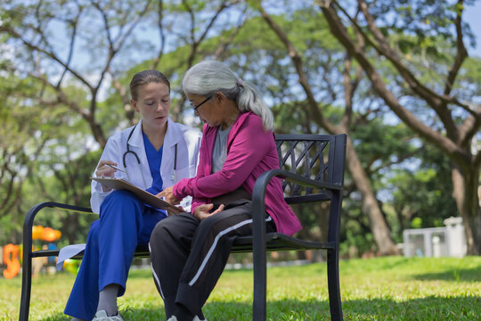 Doctor consulting senior patient outdoors, discussing health report in park