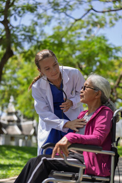 Doctor checking senior woman patient heart in wheelchair outdoors, providing medical care