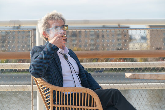 Senior man in eyeglasses smoking cigarette outdoors in city