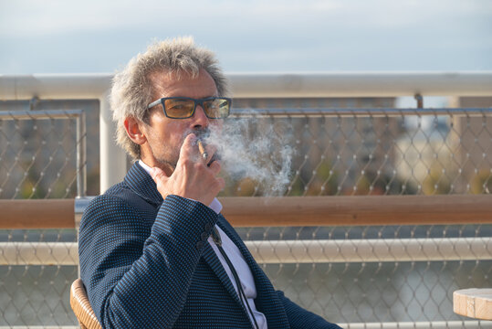 Senior man in eyeglasses smoking cigarette outdoors in city