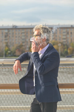 Senior man in eyeglasses smoking cigarette outdoors in city