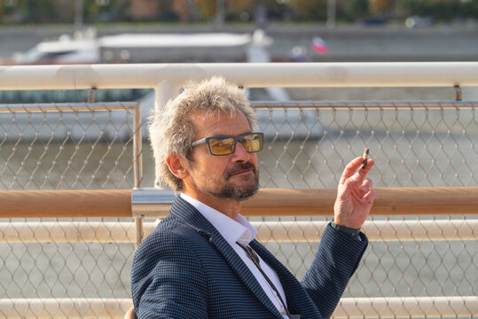 Senior man in eyeglasses smoking cigarette outdoors in city