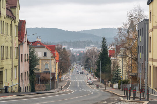 A broad residential street descending through Jablonec nad Nisou, Liberec Region, Czech Republic, with houses, trees and wooded hills in the distance.