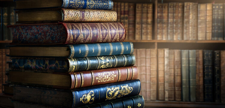 Stack of antique books with richly decorated leather bindings, gilt tooling, raised bands and ornate embossed spines, displayed against a warm old library background. 