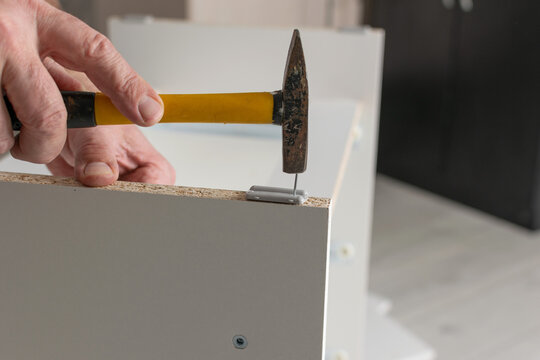 Hands Assembling Furniture with Hammer on White Panel in Home Setting