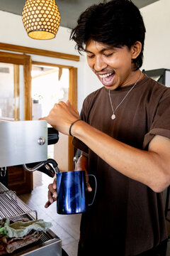 Smiling Indonesian barista steaming milk in local coffee shop