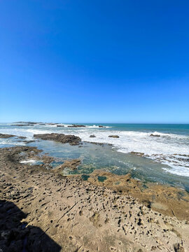 Rocky Atlantic ocean shore at low tide, Essaouira, Morocco. Shallow tidal pools, distant waves and blue sky