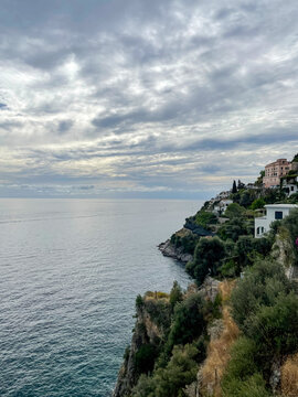 Amalfi Coast cliffs Italy. Houses perched above calm blue sea, cloudy dramatic sky