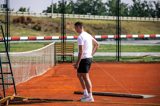 Tennis court groundskeeper pulling a maintenance mat across a red clay court
