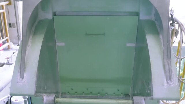 Low angle view of a hopper door opening and tilting on an industrial rubber mixing machine in a rubber band factory