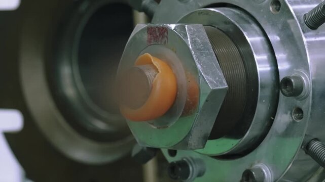 Close up of an orange rubber tube emerging from the die head of an extruder during rubber band manufacturing