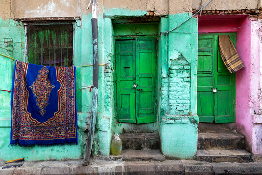 Two green doors beside a window hung with a blue patterned rug on a pastel painted wall, West Bengal, Kolkata, India