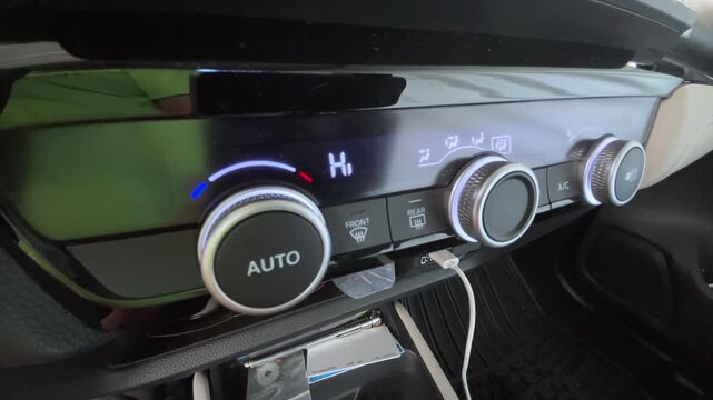 Hand adjusting car climate control temperature dial with automatic air conditioning controls and digital display visible on dashboard inside vehicle interior