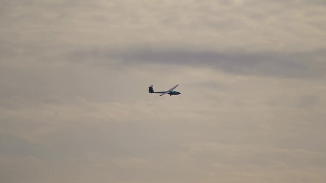 A lightweight glider aircraft flying smoothly in the sky above the airfield. The engineless plane maintains steady flight during a calm day.