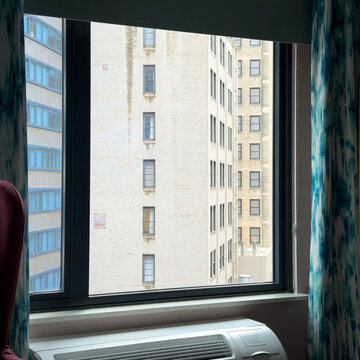 CHICAGO, IL, JUN 17, 2026: Hotel room window with teal curtains and a wall air conditioner, looking out at pale brick buildings and a blue glass facade