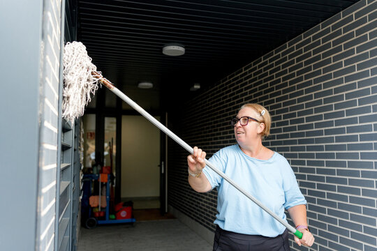Housekeeper clean exterior wall with long-handled mop