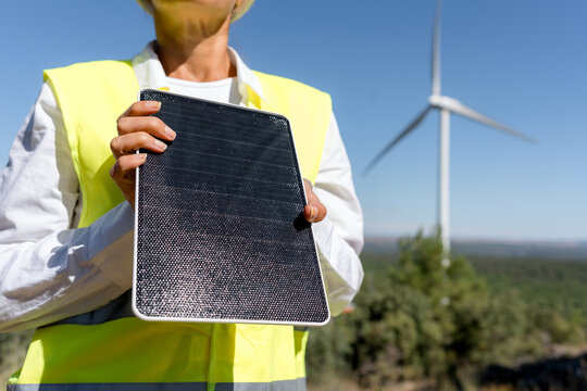Woman engineer hold solar panel near wind turbine