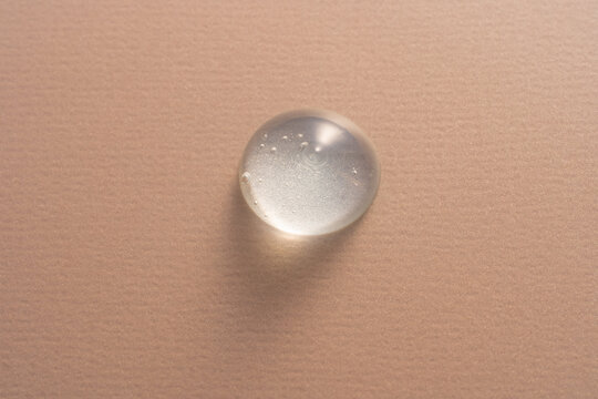 Clear gel drop on textured beige canvas background