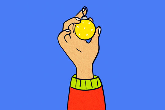 Hand holding yellow Christmas ornament on blue background