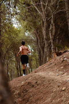 Shirtless runner ascend forest trail during outdoor workout