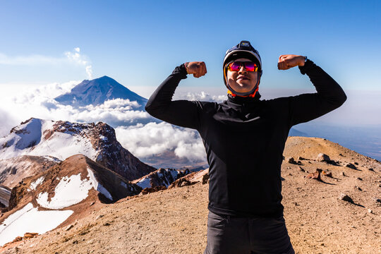 Hiker flexing on snowy mountain summit above clouds