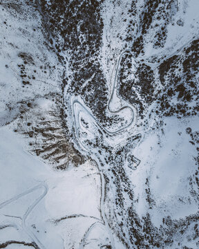 Overhead view of a winding road with sharp switchback curves across snowy mountain slopes