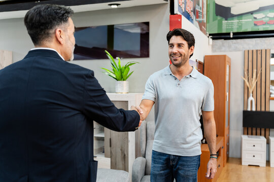 Happy customer and salesman shaking hands in a furniture store, finalizing an agreement on a purchase