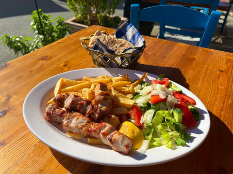 Close up of traditional Greek cuisine. Grilled pork souvlaki skewers served on a plate with french fries, fresh vegetable salad with tomatoes, cucumbers, onions, pita bread, and tzatziki sauce.