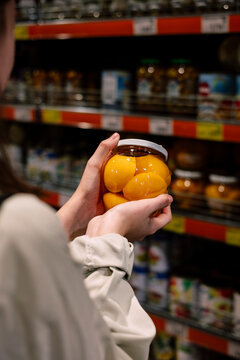 Close-up of a shopper holding a glass jar of canned peach halves.