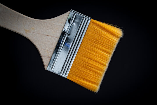 Orange paint brush with wooden handle closeup on black background. Paintbrush with yellow synthetic bristle and metal ferrule. Concept of renovation house painting creative art and DIY repair tool