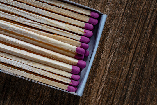 Matches with pink heads in cardboard box closeup. Top view of wooden matches with purple sulfur heads inside a matchbox. Row of matchsticks on dark background for conceptual design or marketing