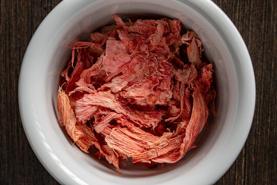 Dried red ginger fibers inside white ceramic bowl. Top view candied red ginger slices in round porcelain cup. Dehydrated sweet ginger root pieces on dark wood background for healthy snack marketing