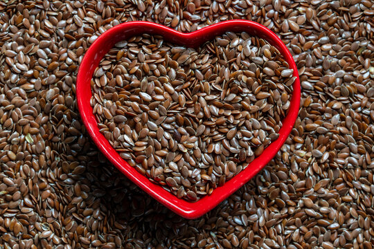 Flax seeds in heart shaped red bowl top view background. Linseed heap with heart shaped ceramic dish. Concept healthy eating, cardiovascular wellness, organic superfood ingredient and love for diet