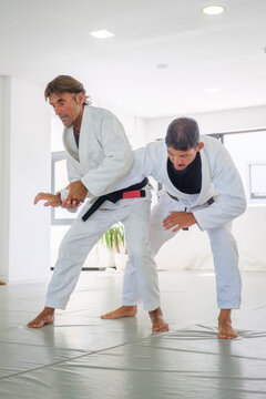 A jiu jitsu instructor controls the straight arm of his partner under his armpit during a standing waki gatame armlock drill on the tatami