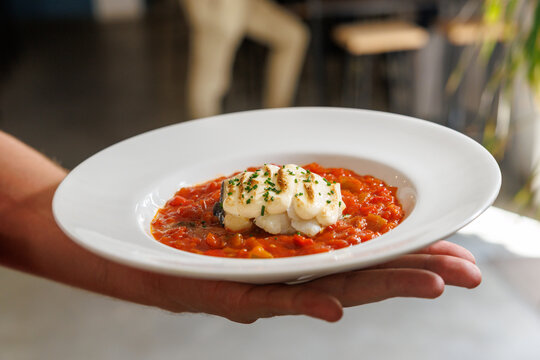Hand serving grilled fish with tomato pepper sauce