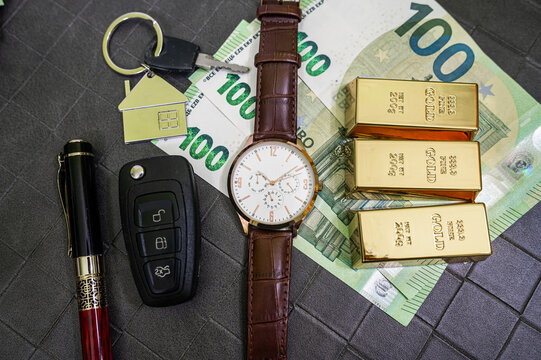 Top View of Men Gold Watch Two Gold Bars 100 Euro Bills House Key Car Key and Smartphone Desk