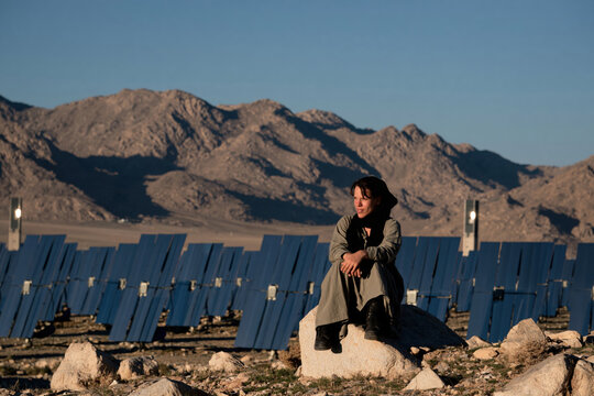Woman sitting on rock in front of desert solar thermal mirror field.