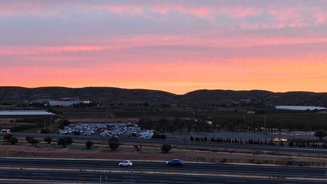 Pink and orange sunset sky over silhouetted desert hills, distant buildings