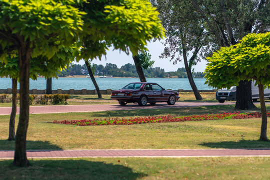 Red classic BMW 635 CSi E24 coupe oldtimer car parked near lake shore framed by trees in Palic, Serbia, Jul 6, 2025