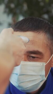 A man is having his temperature checked with a digital thermometer. The man is wearing a mask and appears to be in a medical or health-related setting.