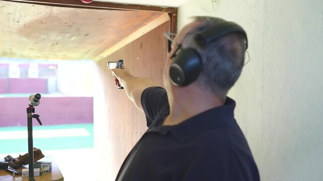 Marksman practicing with a handgun, wearing safety headphones and glasses at an indoor shooting range